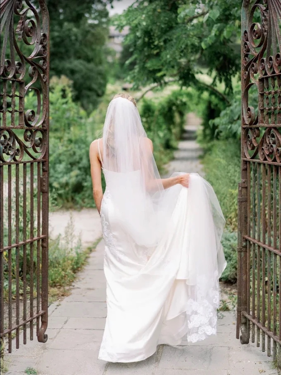 Bride walking through a garden gate in a fitted wedding gown
