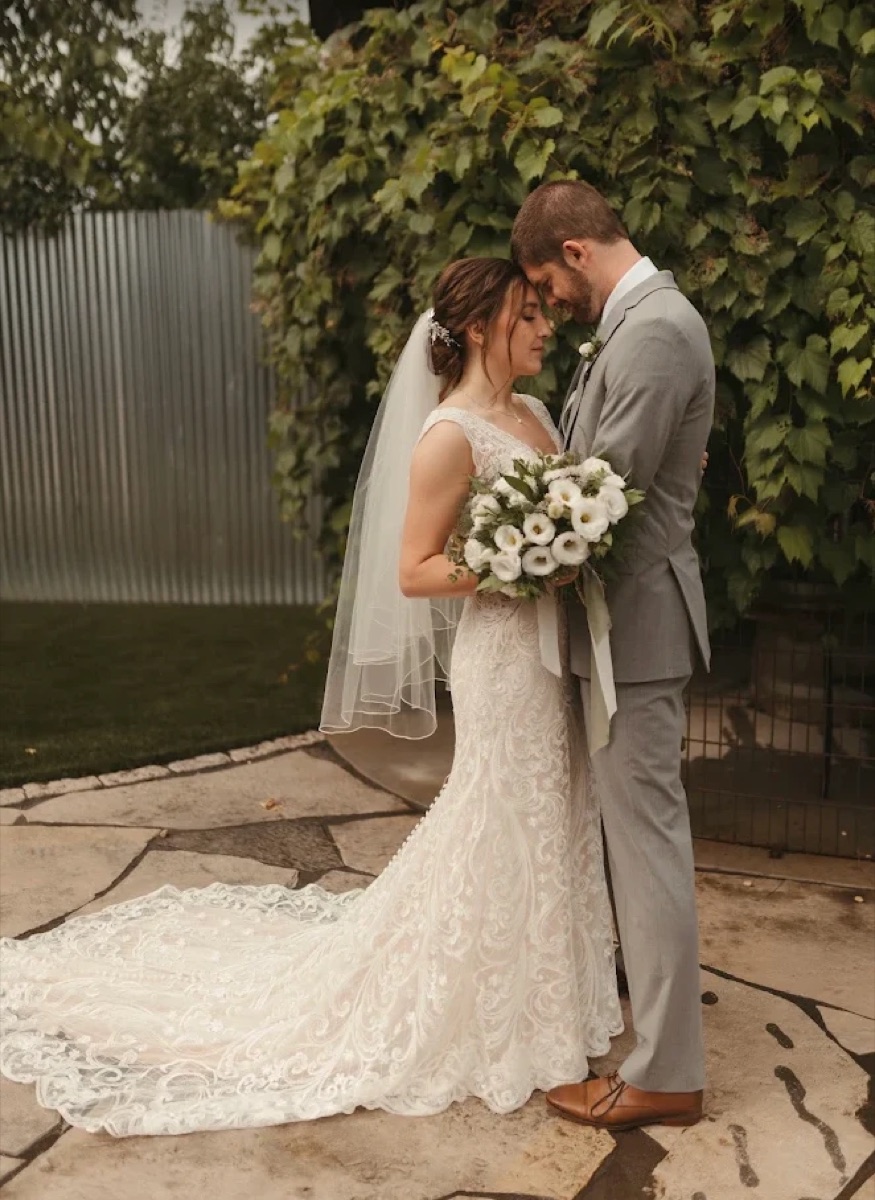 Bride and groom embracing in front of a green ivy wall