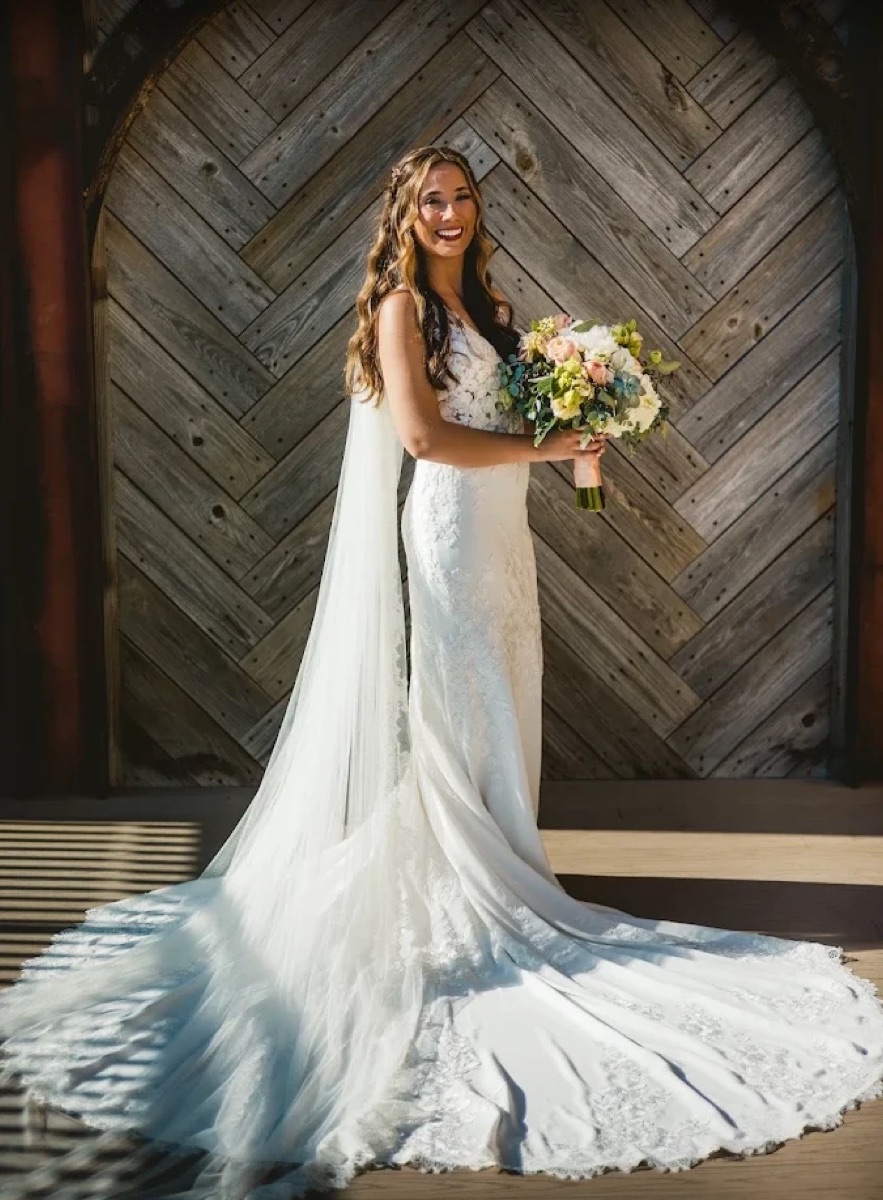 Bride smiling and holding a bouquet in front of a wood backdrop
